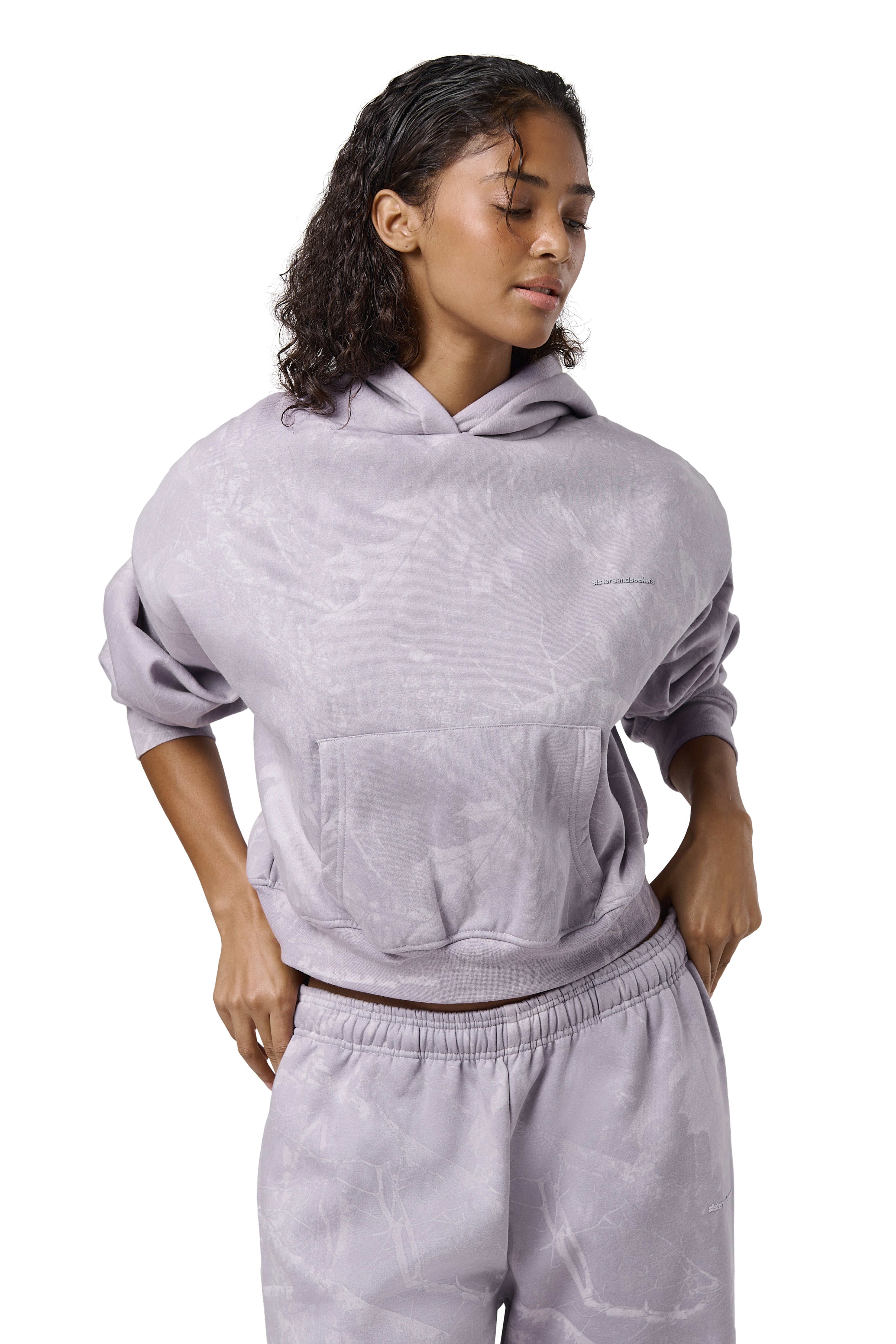 A lilac cropped hoodie with an all-over twig camouflage print, featuring a cropped relaxed fit, dropped shoulders, thick ribbed trims, and embroidered Sisters & Seekers logo.